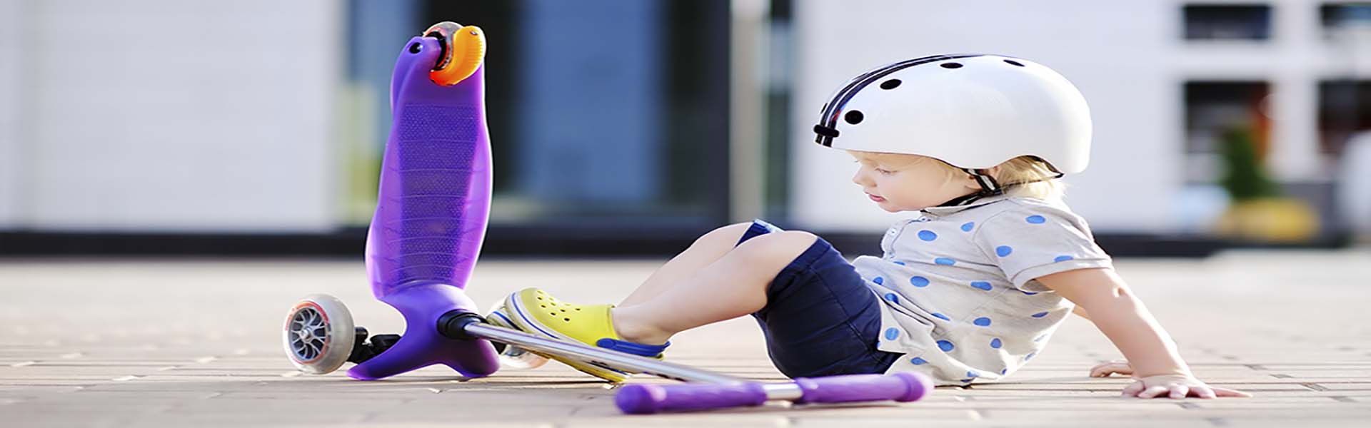 Toddler boy in safety helmet  learning to ride scooter